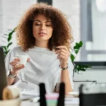 A woman enjoys a coffee break while working in a stylish office space surrounded by plants